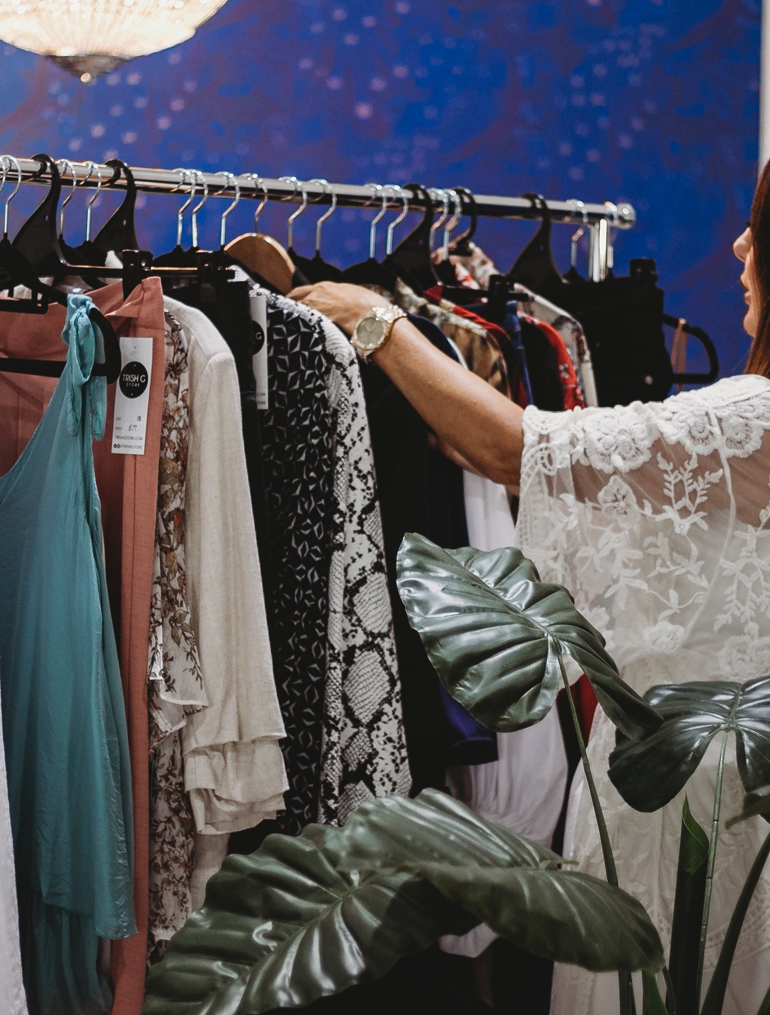 A stylist browses a rack of elegant outfits, curating looks in a stylish, vibrant boutique.