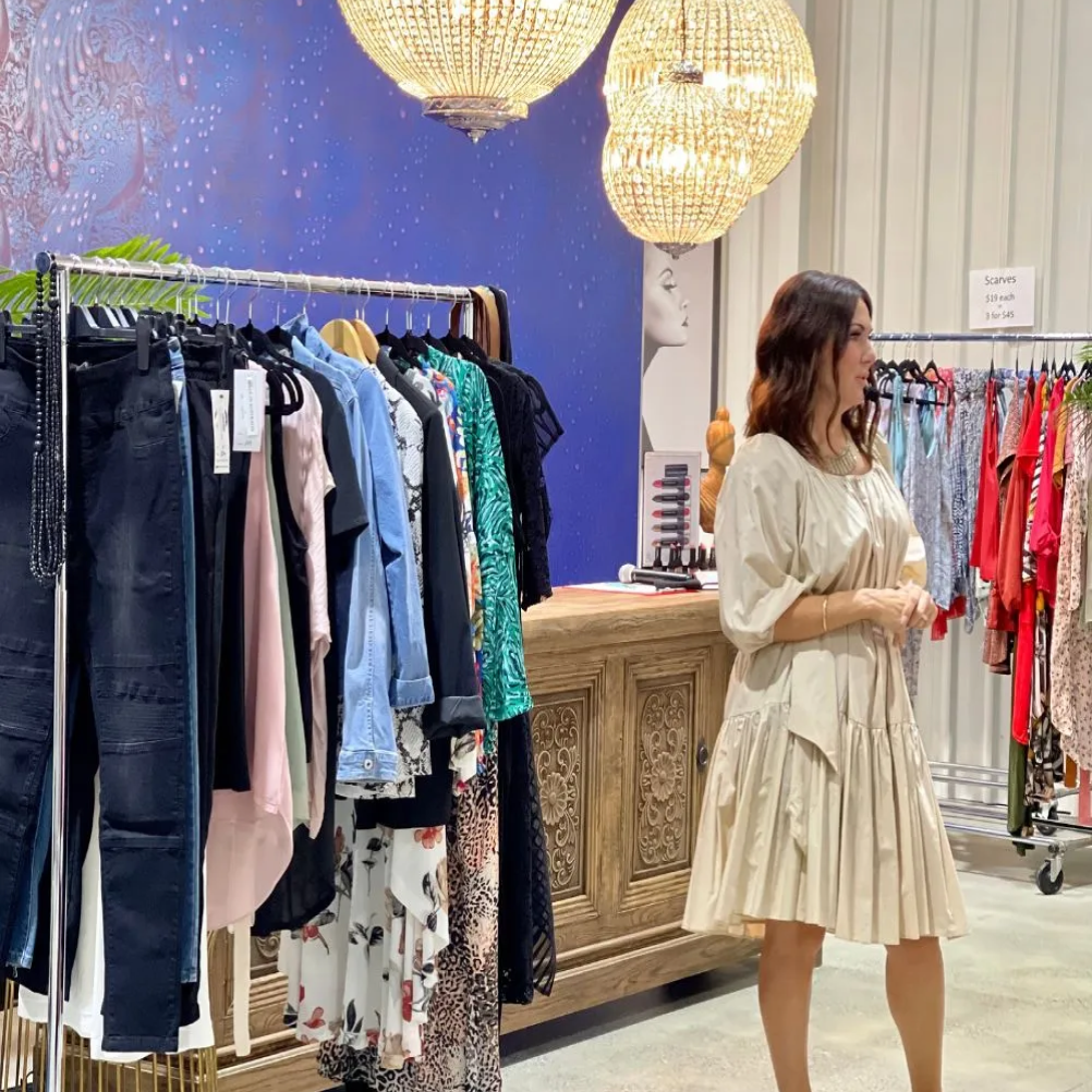 A stylist showcases a neutral-toned dress surrounded by racks of vibrant clothing under stunning chandeliers.