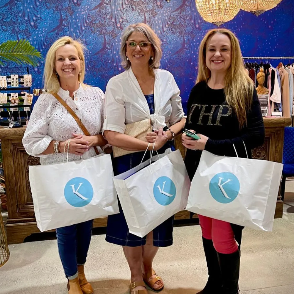 Three women holding shopping bags, smiling in front of a vibrant blue background.