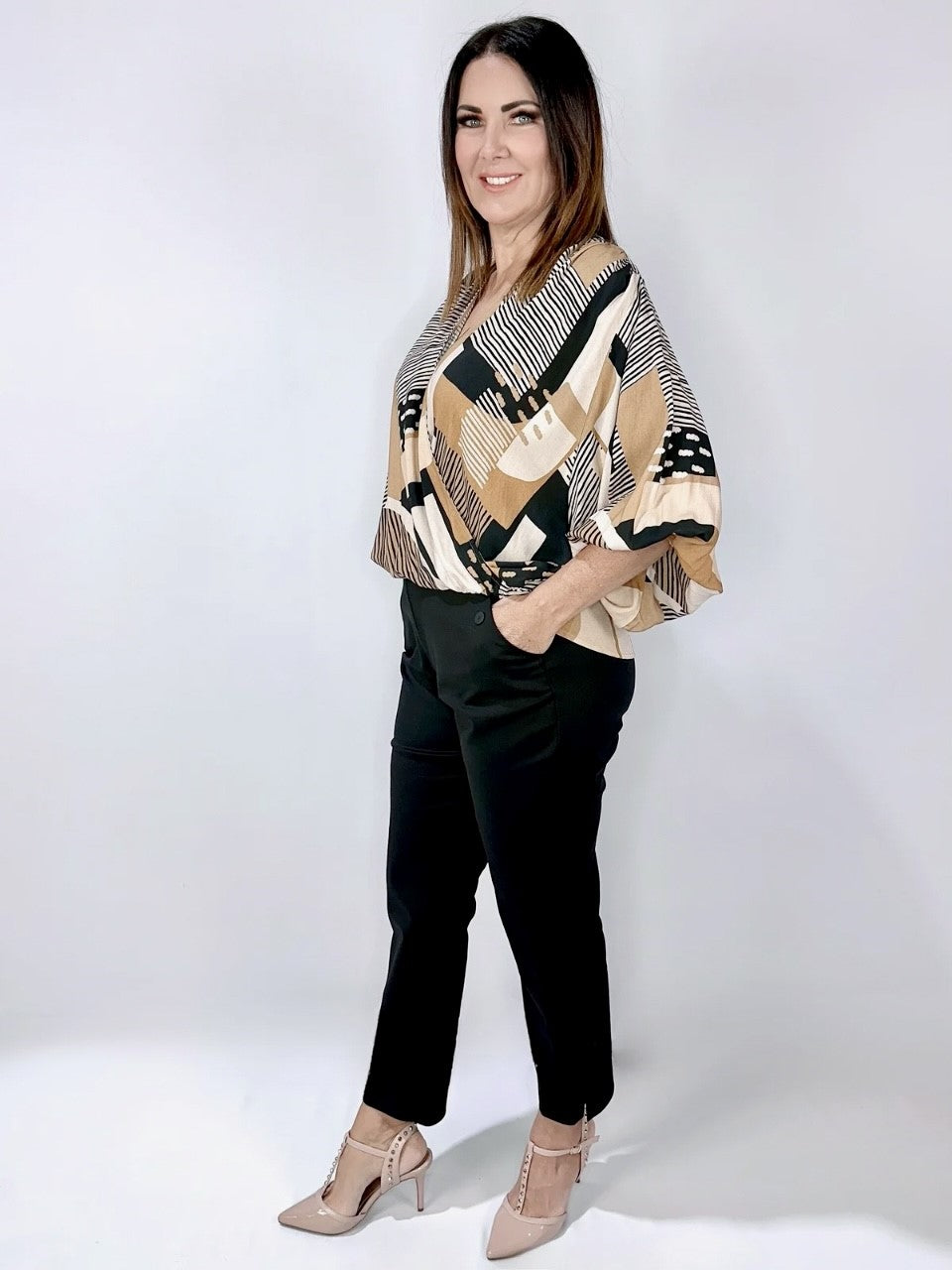 Woman wearing the Sabbia Twist Top with a striped and abstract print, elastic waist, batwing sleeves, and a wrap design.