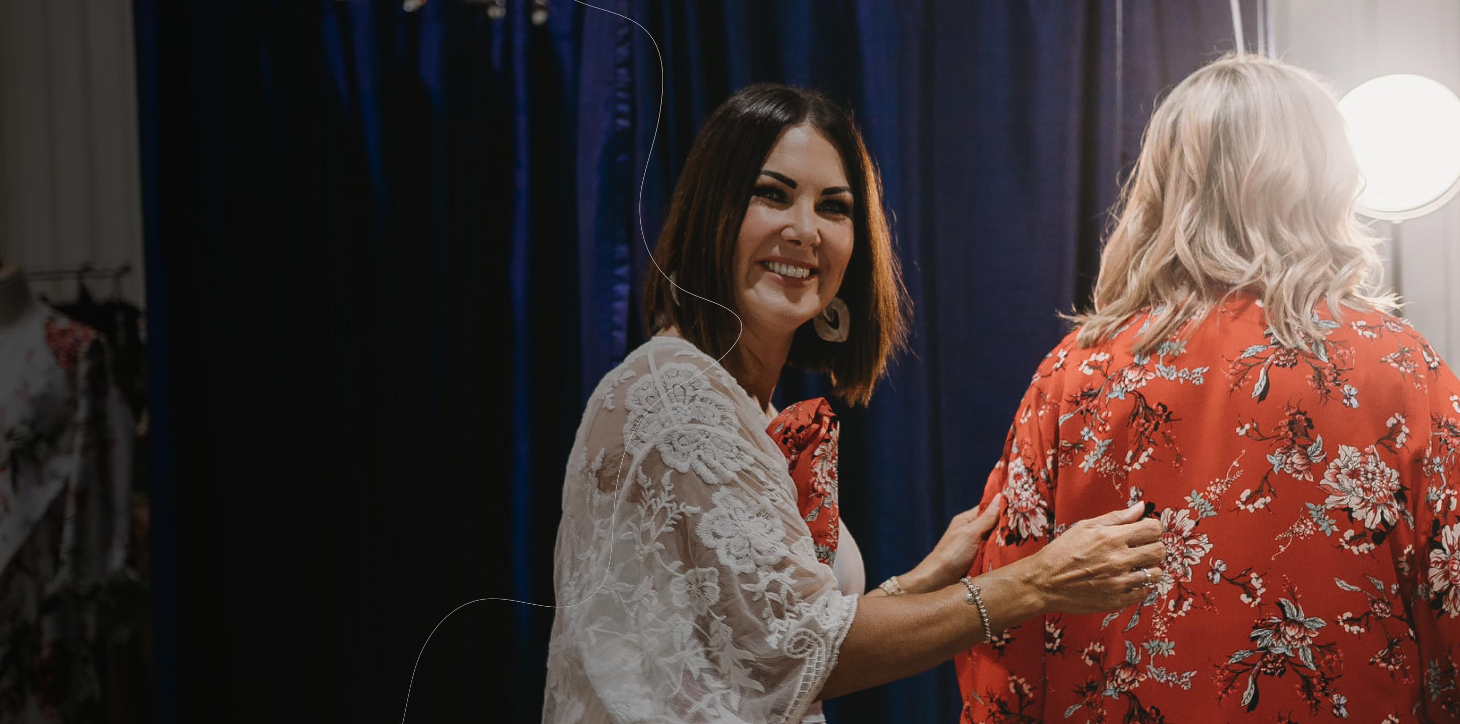 Stylist assisting a client during a fitting session in a floral red kimono.