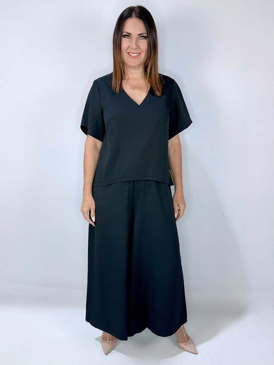 Woman wearing black wide-leg pants with a matching V-neck top, styled with nude heels. The pants feature an elasticated drawstring waist and pockets.