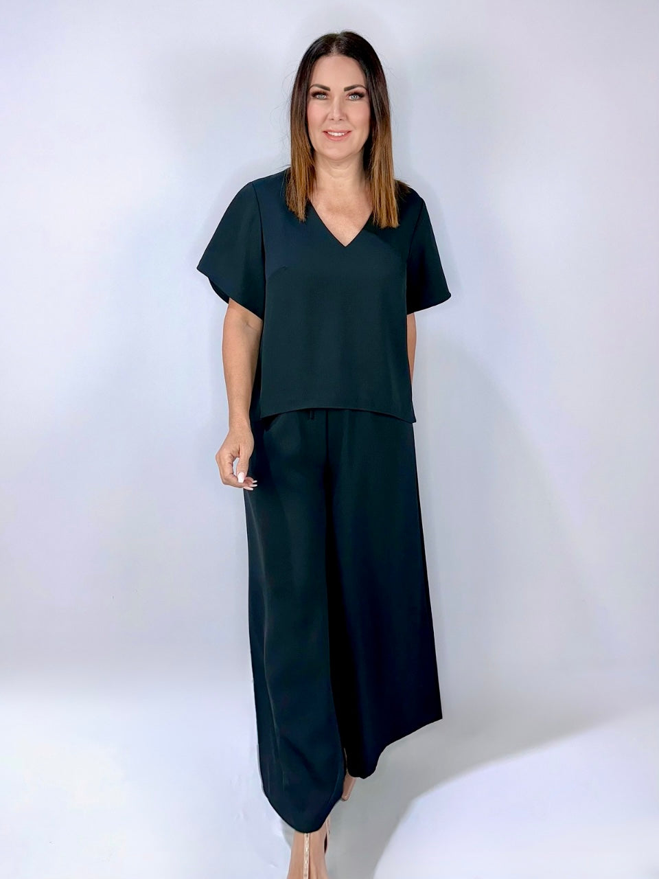Woman wearing Kerry's Style Sessions black short-sleeve V-neck top paired with wide-leg black pants and beige heels.