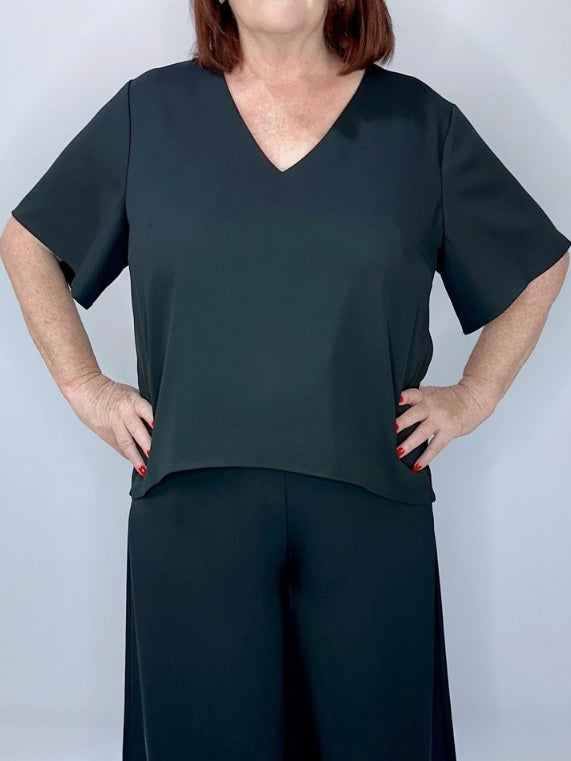 Woman wearing a black short-sleeve V-neck top with matching wide-leg black pants, posing with hands on hips.