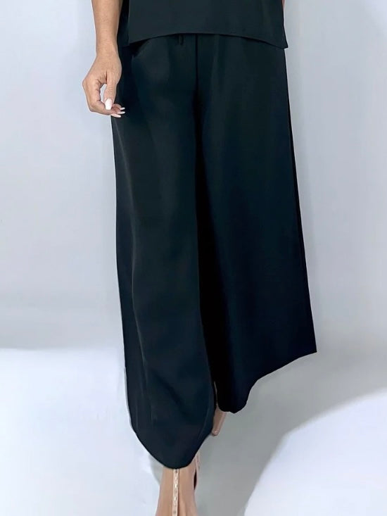 Close-up of black wide-leg pants with a relaxed fit, elasticated drawstring waist, and flowy design, styled with nude heels.