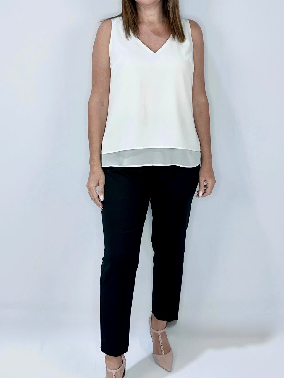 Woman wearing Kerry's Style Sessions white sleeveless V-neck top with sheer hem, paired with black pants and nude heels.
