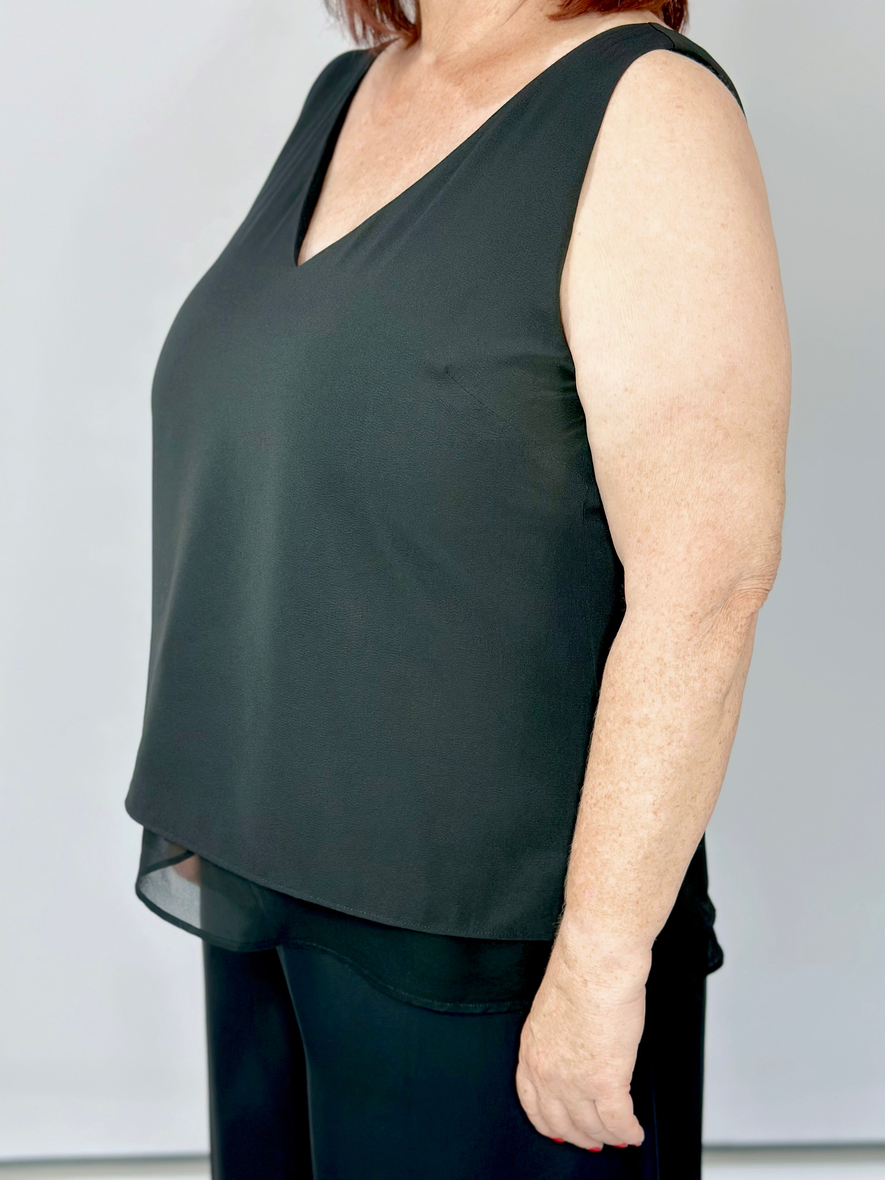 Woman wearing Kerry's Style Sessions black sleeveless V-neck top with a sheer layered hem, paired with black pants.