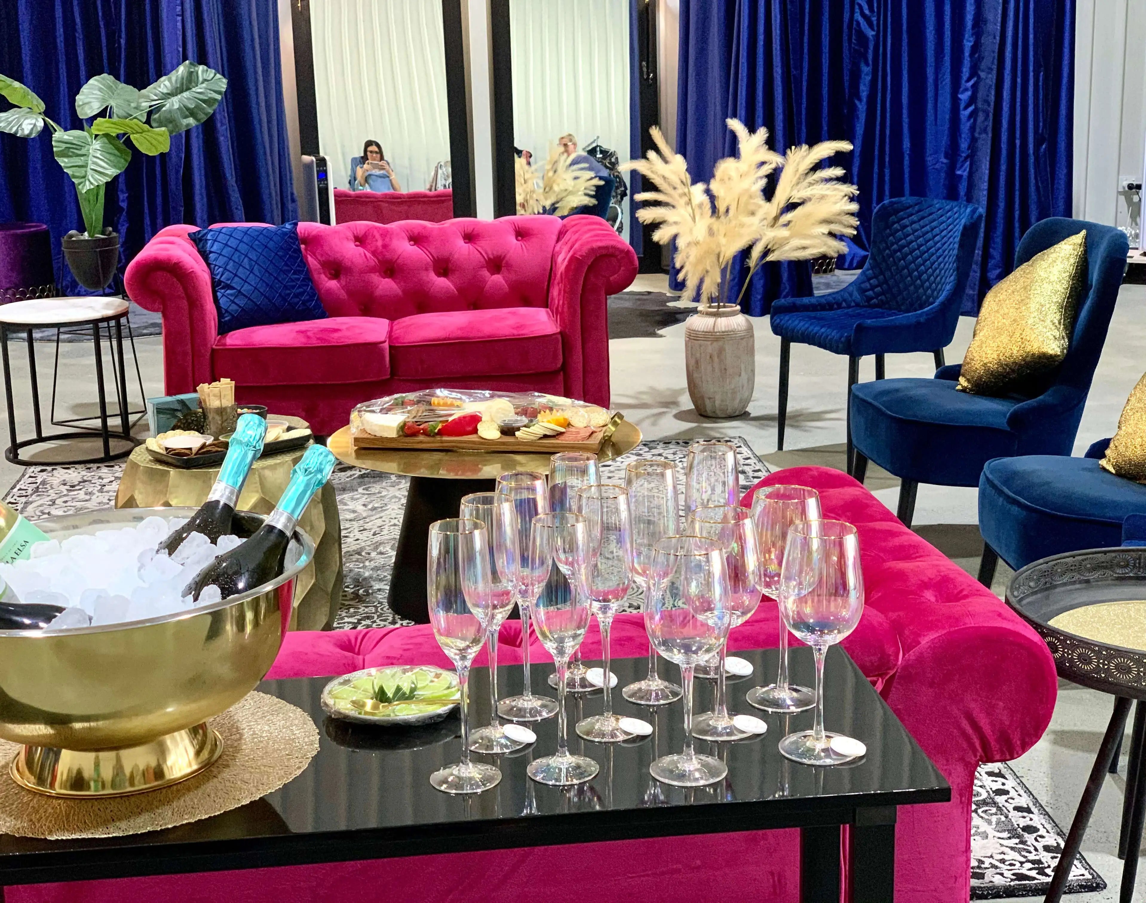 Chic lounge setup with vibrant pink and blue seating, champagne, and elegant glassware, perfect for a stylish gathering.